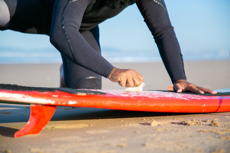 Male surfer in wetsuit waxing surfboard